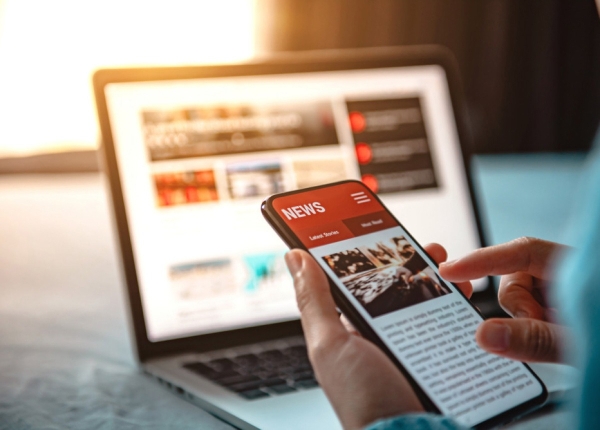 Reading news online: Person using smartphone and laptop for digital news consumption.