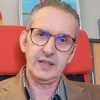 Portrait of a mature man with glasses, wearing a blazer, seated in a red office chair.