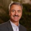 Professional head and shoulders portrait of a mature gentleman with a moustache wearing a grey suit jacket.