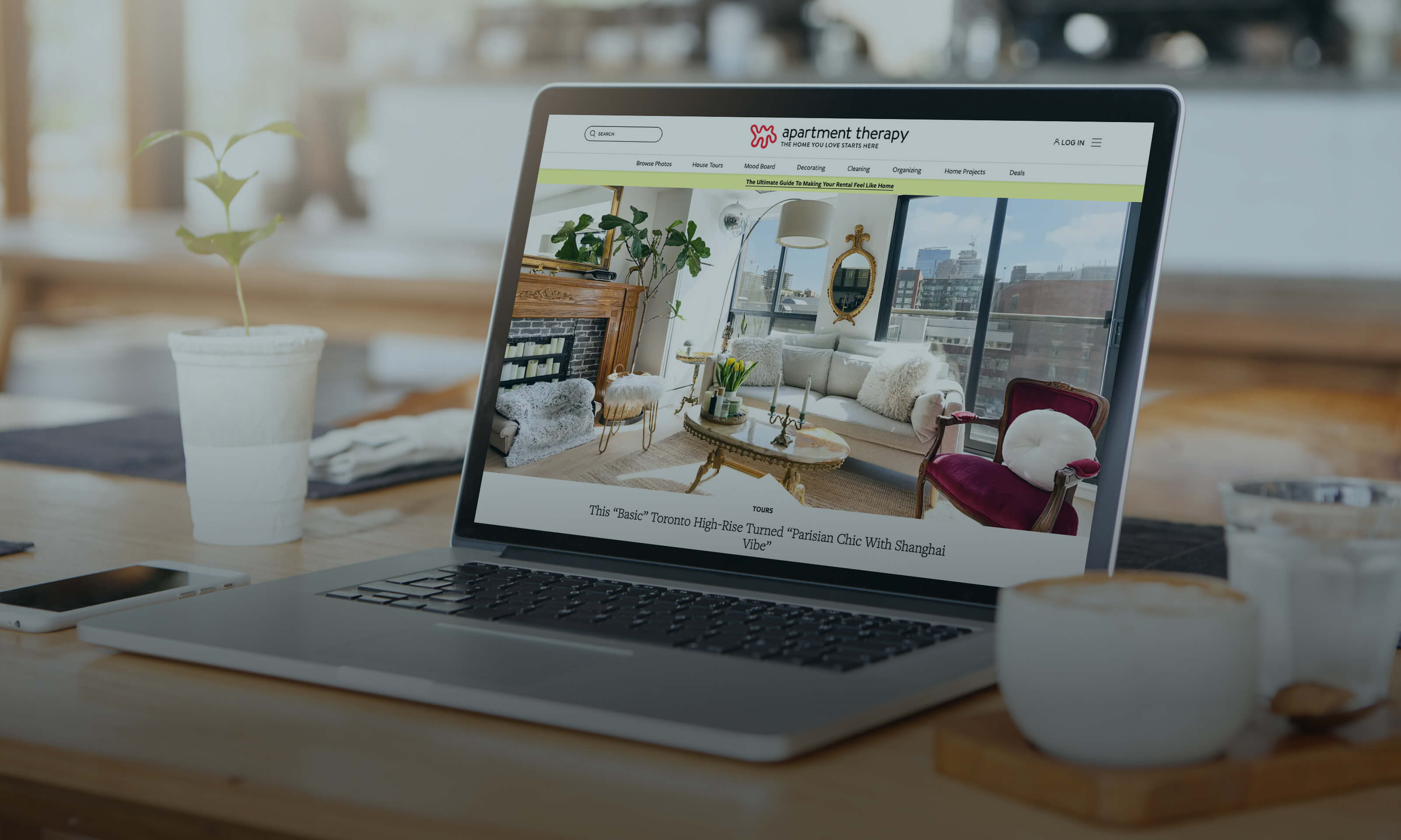 Laptop displaying interior design website with living room photo, coffee cup on desk.