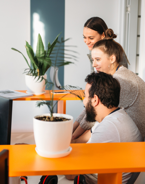 Team-Kollaboration: Drei Kollegen arbeiten gemeinsam an einem orangefarbenen Schreibtisch in einem modernen Büroraum.
