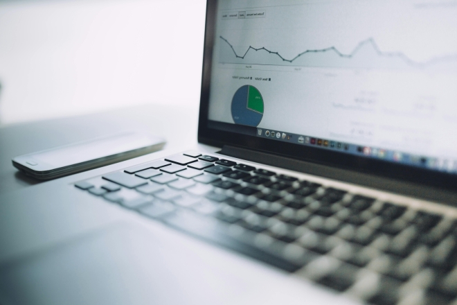 Laptop-Bildschirm mit Datenanalyse-Diagrammen, Tastatur und Smartphone.