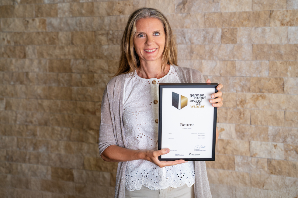 Frau hält Urkunde für die Auszeichnung "Women to Watch in Real Estate" vor einer Ziegelmauer.