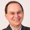 Head and shoulders shot of a middle-aged man wearing glasses, smiling. Professional portrait for business or author profile.