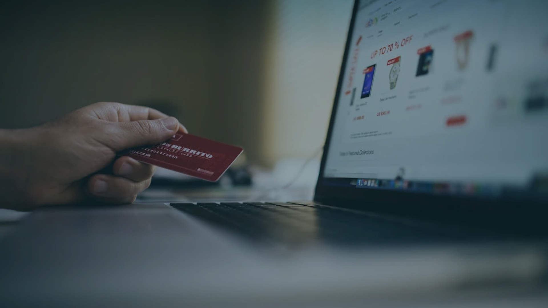 Online shopping with a credit card: Hand holding card near laptop displaying an e-commerce website.