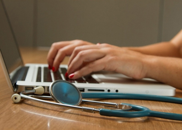 Doctor typing on laptop with stethoscope on desk; telehealth, healthcare technology.
