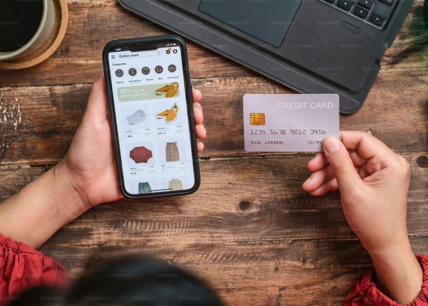 Online shopping: A woman's hands holding a credit card and smartphone displaying an e-commerce app, on a wooden desk.