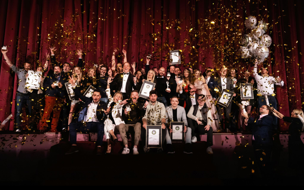 Large group celebrating award ceremony on stage with confetti and balloons.