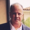 Professional headshot of a mature man in a suit jacket and white shirt outdoors.