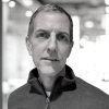 Black and white portrait of a mature man with short hair, wearing a zip-up jacket. Head and shoulders shot for professional profile.