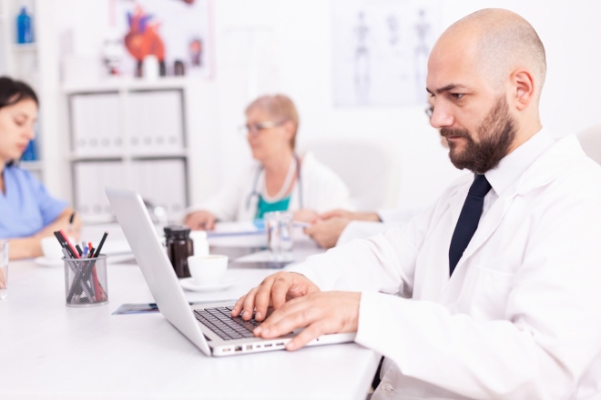 Arzt mit Laptop im Arztzimmer mit Kollegen. Besprechung des Gesundheitsteams.