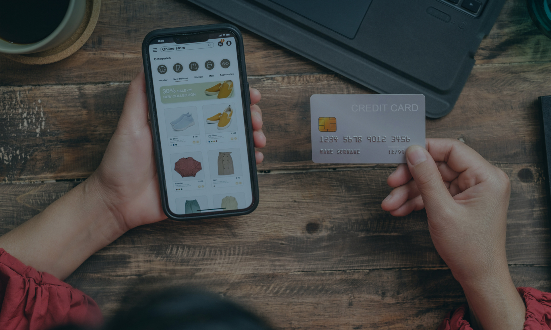 Online-Shopping mit Kreditkarte auf dem Smartphone; Frauenhände, Holztisch, Laptop.