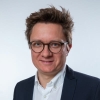 Professional head and shoulders portrait of a man wearing spectacles, a navy blazer, and a white shirt.