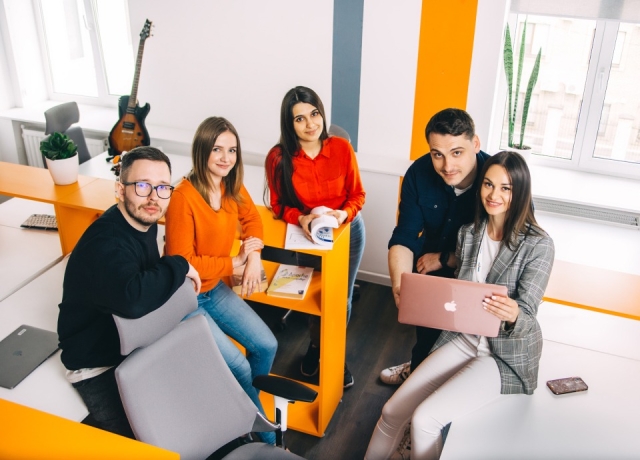 Vielfältiges Team junger Berufstätiger arbeitet in einem modernen Büroraum mit Laptops zusammen.