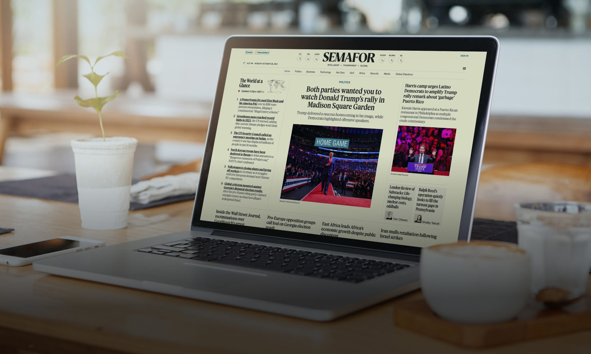 Laptop displaying the Semafor news website on a wooden table with coffee and plant.