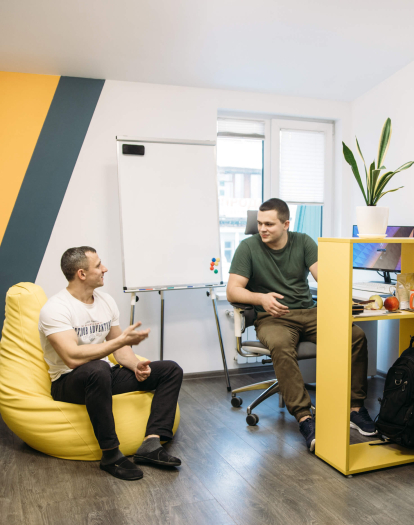 Zwei Männer in einem modernen Büro: Einer sitzt in einem gelben Sitzsack, der andere an einem Schreibtisch.