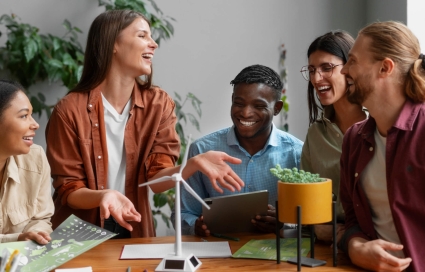 Ein diverses Team sitzt lachend um einen Tisch mit einem Windturbinenmodell und diskutiert nachhaltige Energielösungen.
